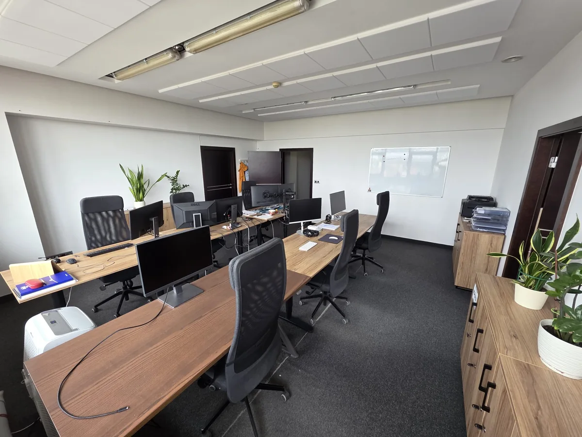 Otwarta sala coworkingu Mini Office z biurkami, drewnianymi regałami i roślinami